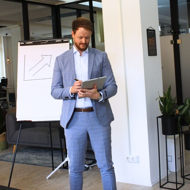 Marketingberater im hellblauen Anzug steht mit einem Tablet in der Hand im Konferenzraum und blickt auf Marketingdaten