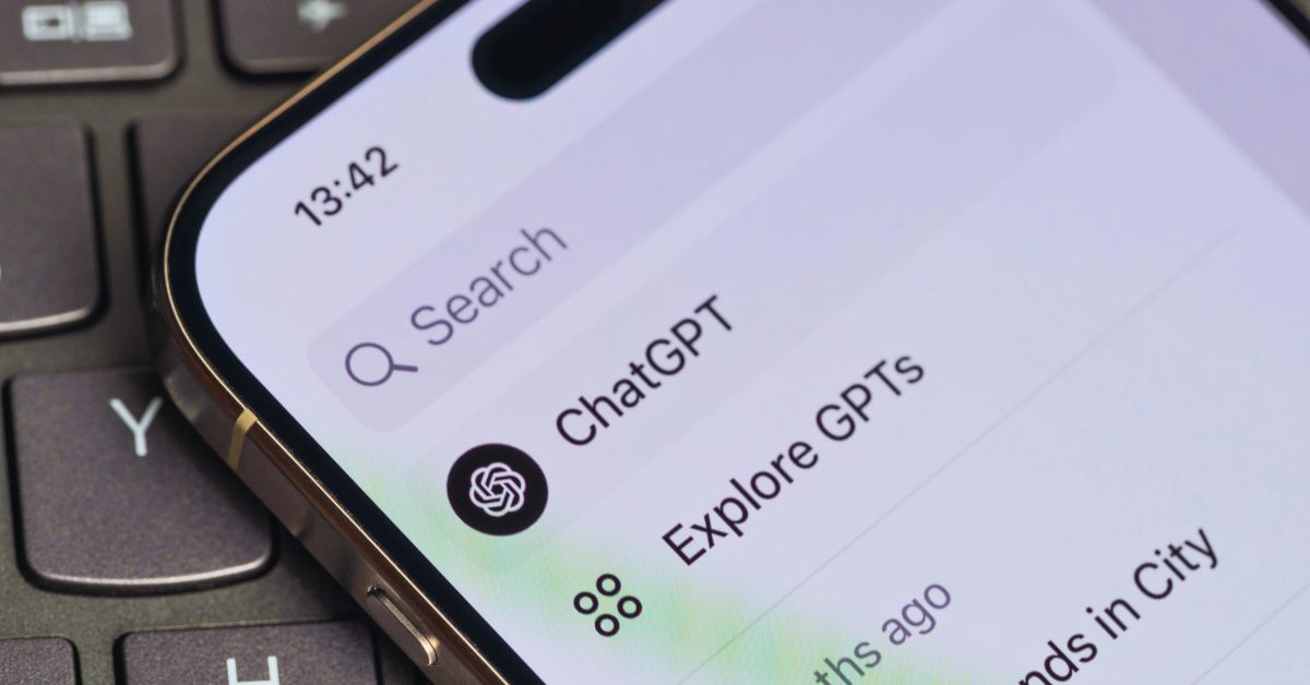 Nahaufnahme eines Smartphones mit offener ChatGPT-App auf einer Laptoptastatur
