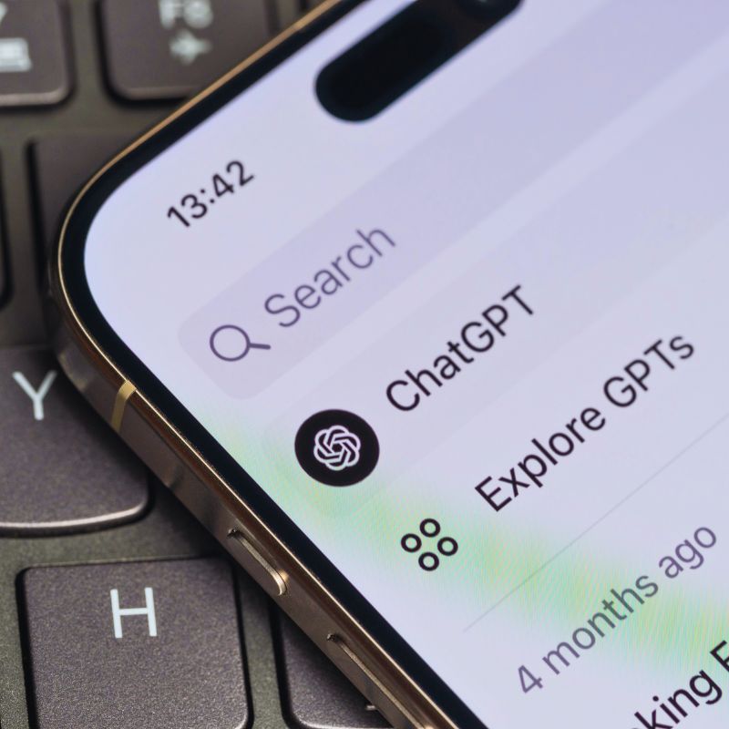 Nahaufnahme eines Smartphones mit offener ChatGPT-App auf einer Laptoptastatur